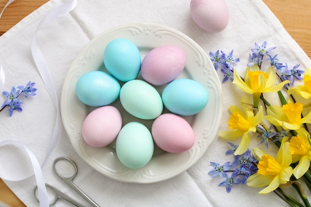 Easter table with colorful eggs on a plate and a bouquet of daffodils