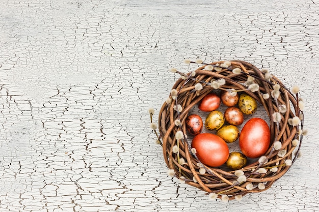 Easter willow wreath and colorful Easter eggs on white table. Top view, copy space