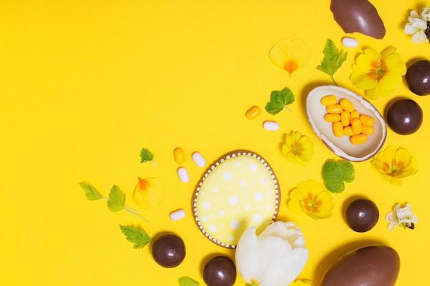 Easter yellow background with chocolatte eggs    candy and spring flowers