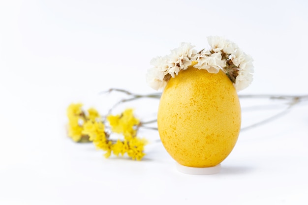 Easter yellow egg with wreath and wildflowers on white background