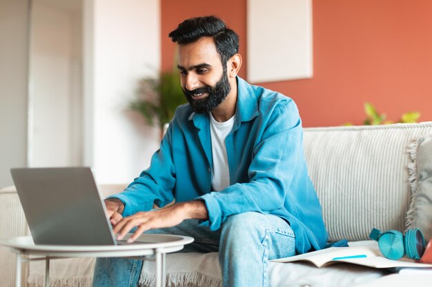 Eastern man in casual using laptop typing in living room