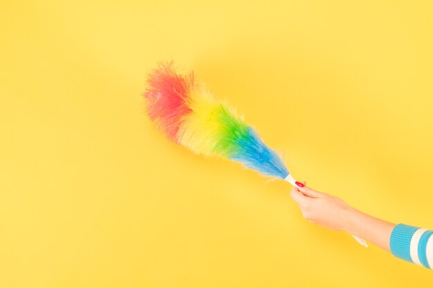 Easy dust cleaning. Woman hand with feather duster. Copy space on yellow background.