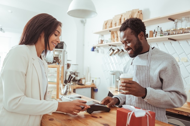 Easy and fast. Pleasant female customer pressing her mobile phone to the credit card terminal and making a payment for her order via NFC technology