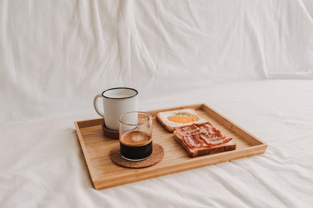 Easy simple breakfast set of bacon sandwich served with black coffee on bed