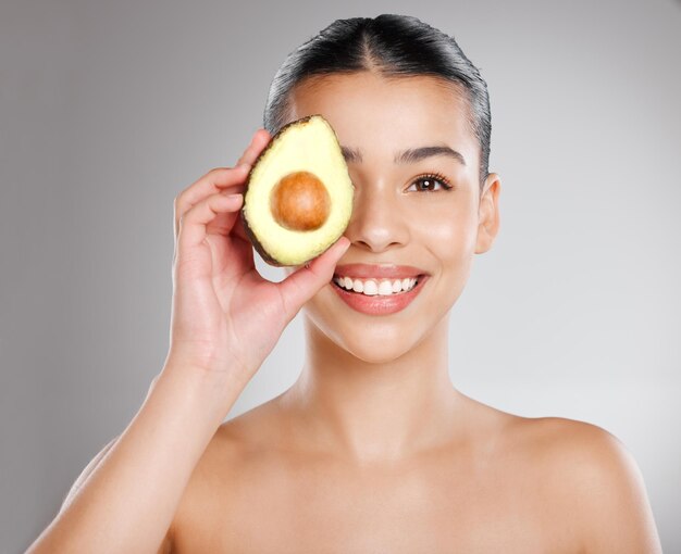 Eat healthy make your skin happy studio shot of an attractive young woman holding an avocado to her