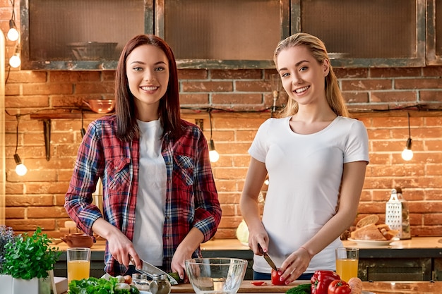 Eat organic for health smiling young women cutting vegetables in modern kitchen cozy interior