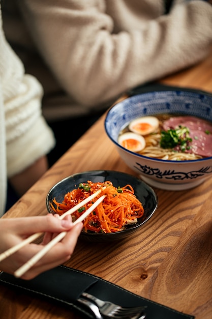 Eating asian marinated carrot and shoyu ramen with chopsticks