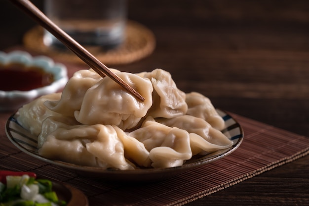 Eating fresh, delicious boiled dumplings, jiaozi on wooden table background with soy sauce