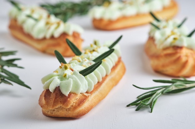 Eclairs with pistachio cream and raspberry filling, garnished with crushed pistachio and rosemary.