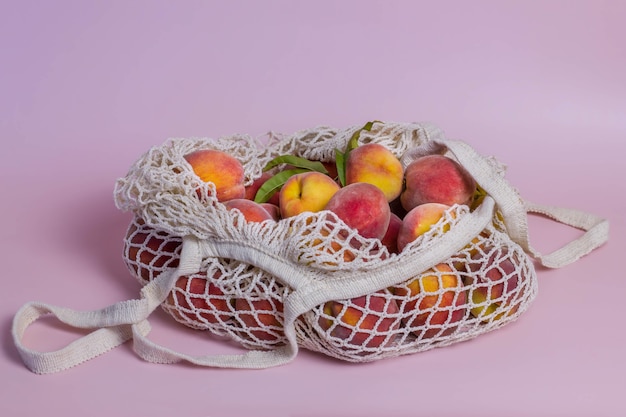 Eco bag with fruits on a pink background. Natural shopping bag with fresh peaches.