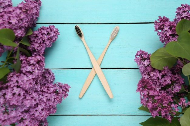 Eco bamboo toothbrushes with branches of blooming lilacs on blue wooden background Spring eco concept Top view Flat lay