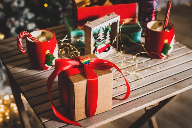 Eco craft box with red bow and lgbt symbol. table decorated for christmas, new year. mugs with cocoa, candy. gift