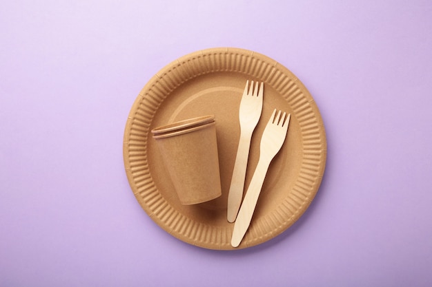 Eco craft paper tableware. Paper cups, dishes, bag, fast food containers and wooden cutlery on purple background. Zero waste. Recycling concept. Copy space