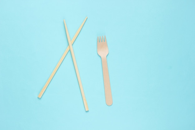 Eco cutlery. Chinese chopsticks, wooden fork on blue background.