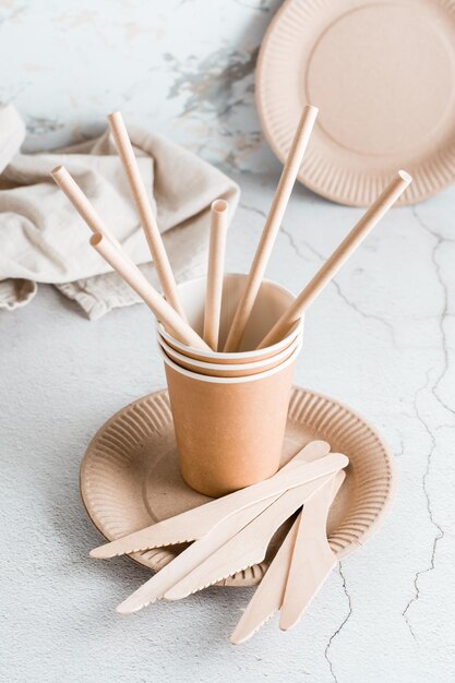 Eco friendly cardboard disposable tableware Plates cups tubules and wooden knives are on the table Vertical view