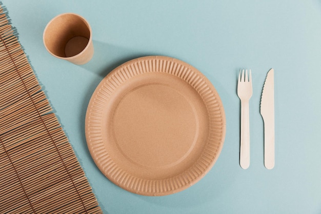 Eco-friendly disposable utensils made of bamboo wood and paper on a light blue background. Plates, fork, knife, paper cups