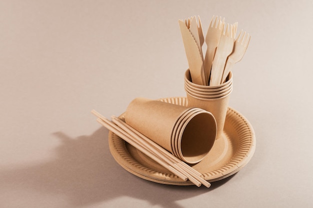 Eco-friendly disposable utensils made of craft paper on a light beige background. Fork, knives, plates, paper cups and straws