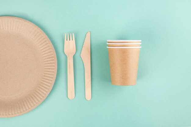 eco-friendly tableware on a blue background, paper plates and glasses, wooden forks and nomes, top view