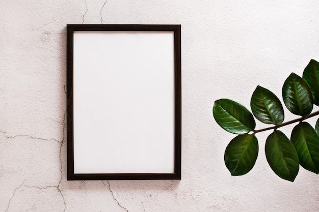 Eco mock up. Empty frame with a blank sheet on a light concrete background and leaves of home plants. Copy space. Top view.