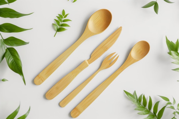 Ecofriendly bamboo kitchen utensils arranged neatly on a white surface decorated with fresh green leaves