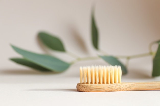 Ecofriendly bamboo toothbrush on a light beige texture closeup with a leaf on the background