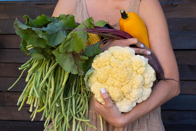 Ecofriendly concept with organic farm vegetables in the hands of a girl in a linen dress of natural fabric Fresh raw cauliflower green beans zucchini corn beets Farm measured life in nature