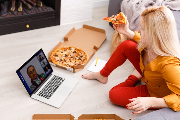 Ecommerce woman. Young female using computer for online shopping, sitting on the floor and eating pizza.