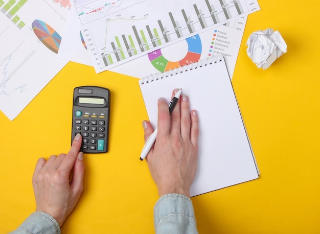 Economic analysis. Female hands count the calculator on a yellow with a notebook, graphs and charts.