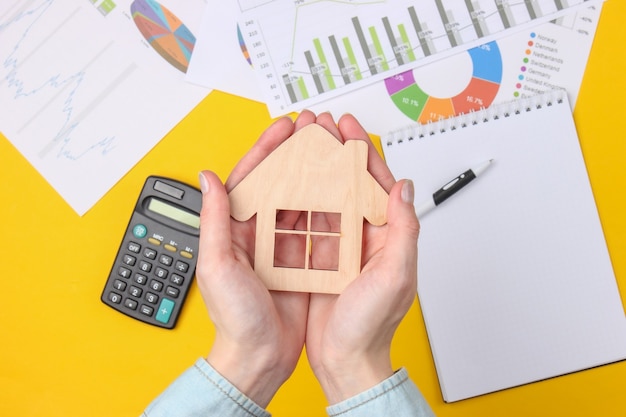 Economic calculation of cost housing. Female hands holding house figure on a yellow with a calculator