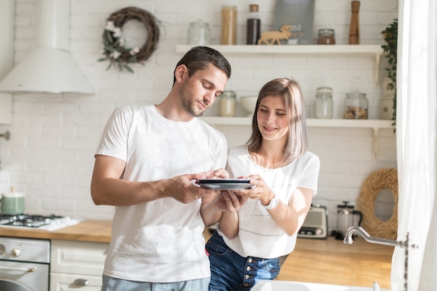 Economic woman washing dishes and handing it to diligent man to wipe in kitchen at home