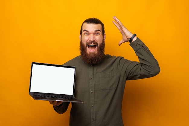 Ecstatic bearded man holding a laptop with blank screen is mind blown