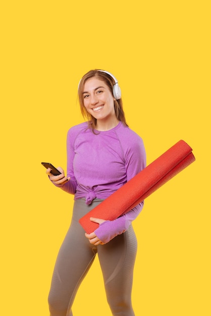 Ecstatic woman is holding a red mat and her phone while looking at the camera