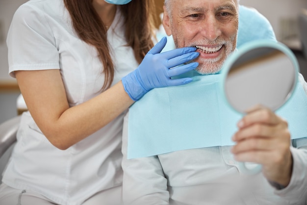 Ederly patient of a dental clinic smiling and looking in the mirror at his fixed teeth