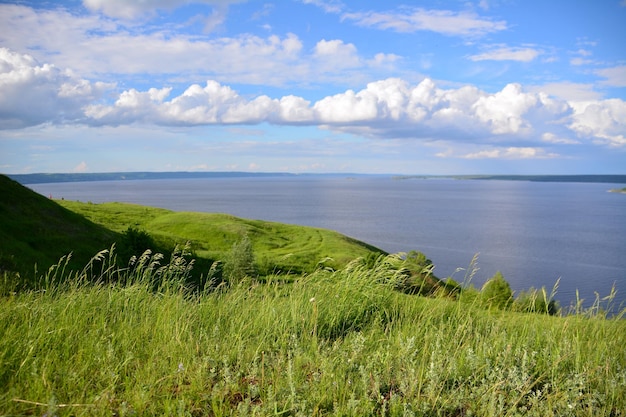 edge of the hill with river and evening sky with white clouds