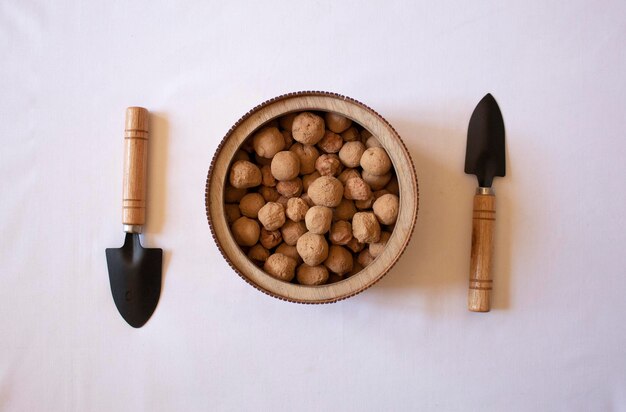 Edible caramel clay stones on a wooden round plate with small garden shovels on a white background