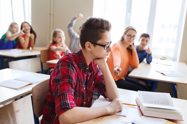 education, bullying, conflict, social relations and people concept - student boy in glasses reading book and suffering of classmates mockery at school