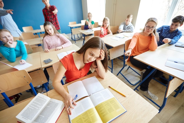 education, bullying, conflict, social relations and people concept - students teasing and judging girl classmate behind her back at school