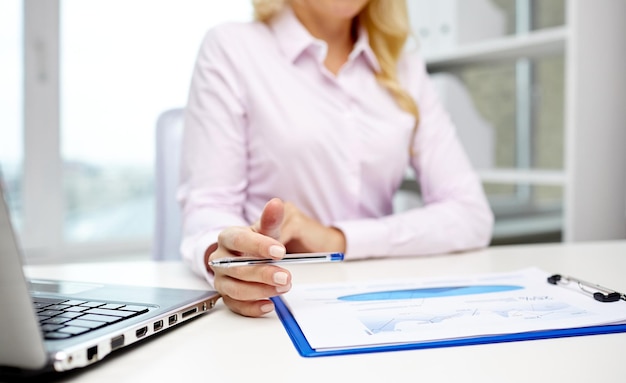 education, business, people and technology concept - close up of smiling businesswoman with laptop computer and papers sitting in office