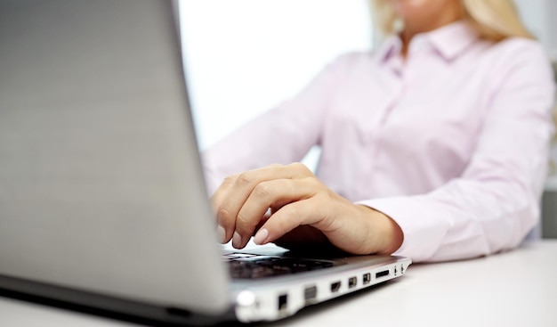 education, business, people and technology concept - close up of smiling woman hands or student with laptop computer typing in office