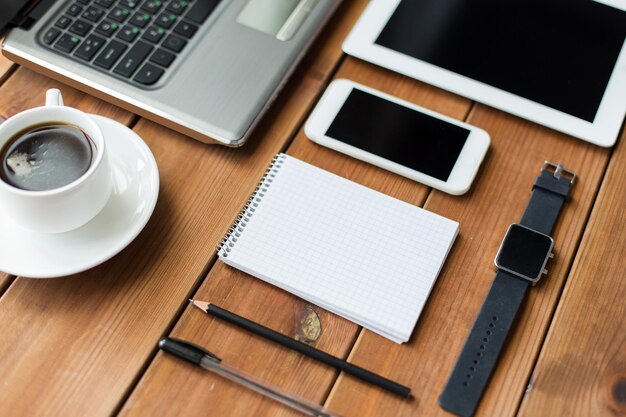 education, business and technology concept - close up of on laptop computer, tablet pc, notebook and smartphone on wooden table