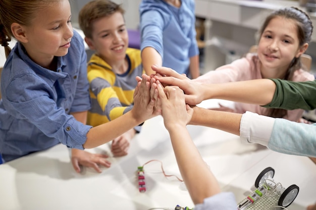 Photo education, children, technology, science and people concept - group of happy kids building robots and making high five gesture at robotics school