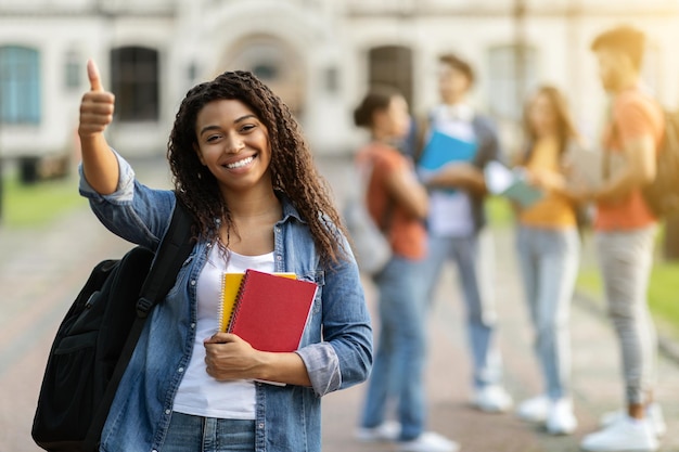 Education concept smiling black female student showing thumb up while posing outdoors