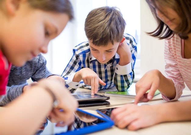 education, elementary school, learning, technology and people concept - group of school kids with tablet pc computer having fun on break in classroom