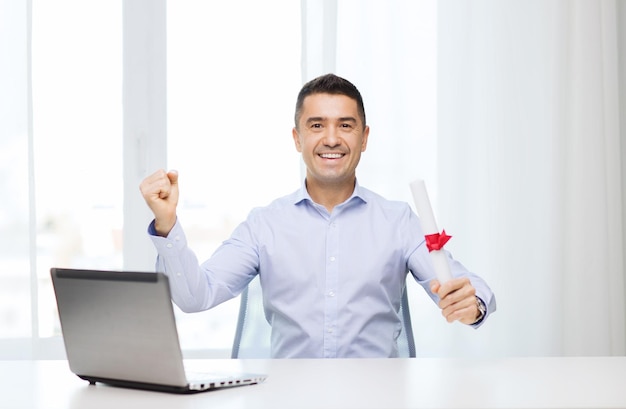 education, graduation, business, technology and people concept - smiling man with diploma and laptop computer sitting showing triumph gesture hand