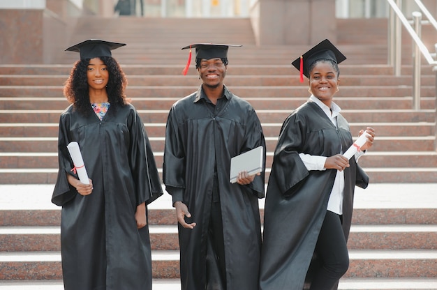 Education, graduation and people concept - group of happy international students in mortar boards and bachelor gowns with diplomas