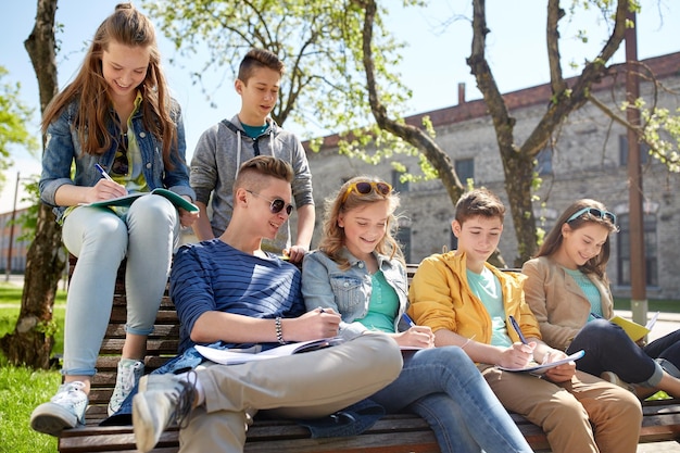 education, high school and people concept - group of happy teenage students with notebooks learning at campus yard