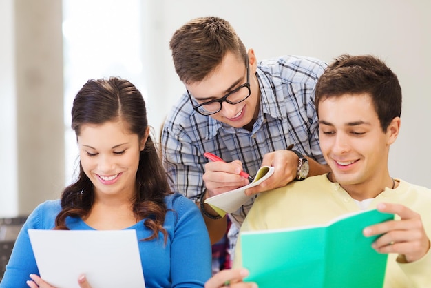 education, high school, teamwork and people concept - group of smiling students with notebook sitting in lecture hall and writing