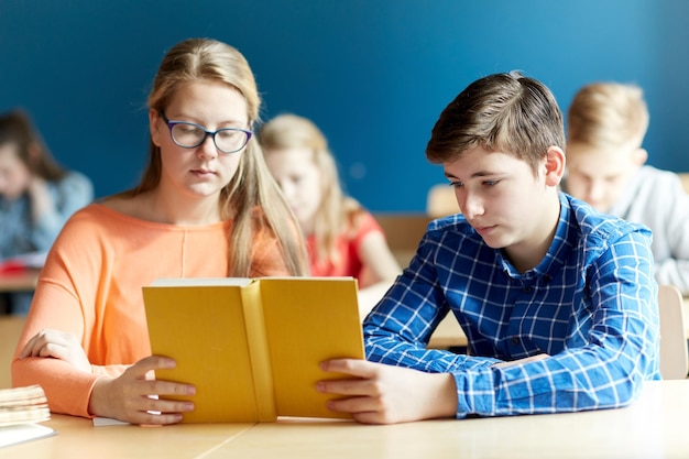 education, learning and people concept - group of students with book reading at school lesson