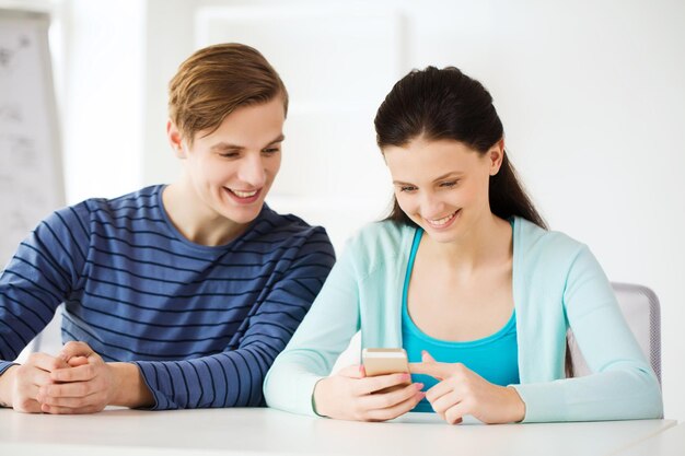 education, relationships and technology concept - two smiling students with smartphone at school