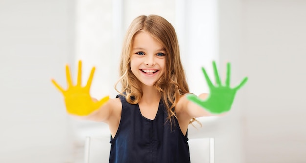 education, school, art and happiness concept - little student girl showing hands in yellow and green color at school